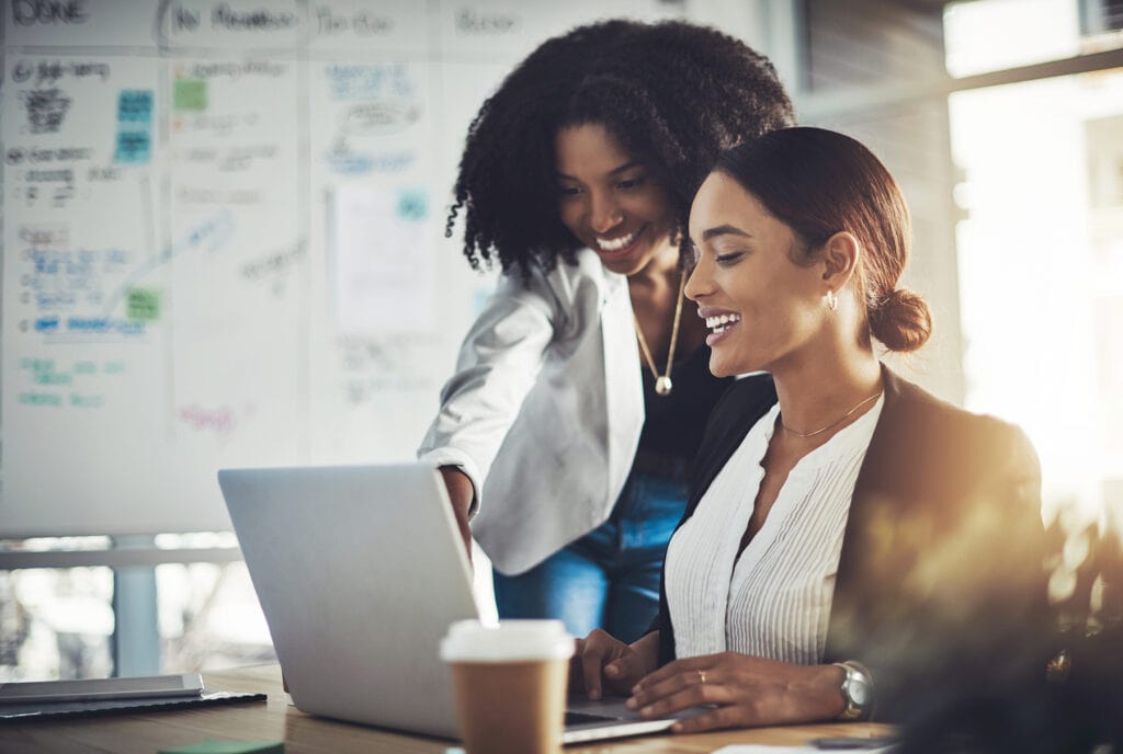 Two women collaborating on a laptop in a modern office setting.